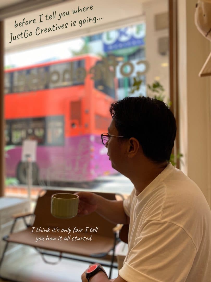 Godfrey at a cafe with a coffee, a red bus passing outside